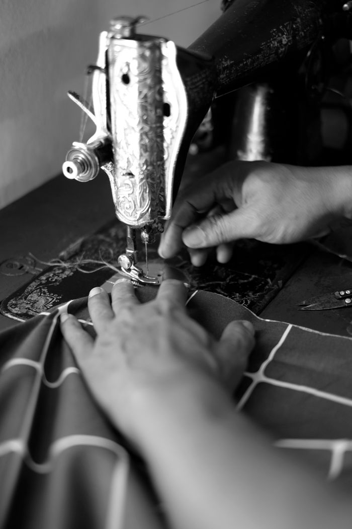 Black and white image of hands operating a vintage sewing machine, creating intricate fabric patterns.
